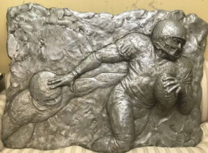 This piece was created for the Falcon's Owner's Club through the Johnson Studio in 2005, by sculptor Martin Dawe of Cherrylion Studios. The piece depicts two football players in relief. Dimensions 4'9
